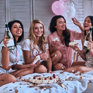 Unforgettable party. Four beautiful young women in pajamas eating cake and drinking champagne while having a slumber party